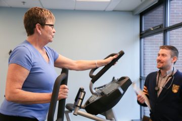 An SSBC coach works with a program participant who is using an elliptical machine
