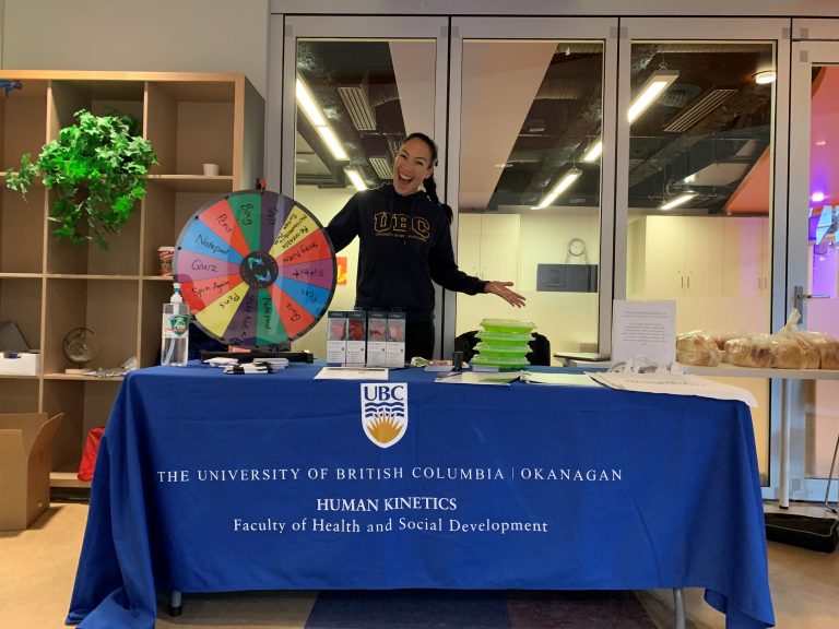 Dr. Mary Jung behind a UBC booth with a prize wheel